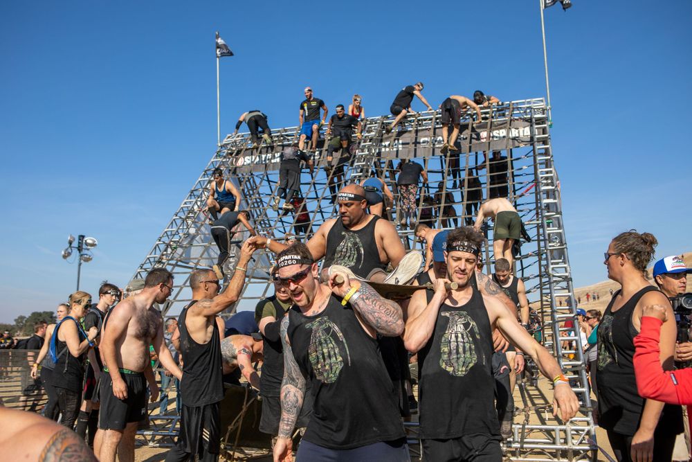 Large group of athletes celebrating at the top of a metal climbing structure.