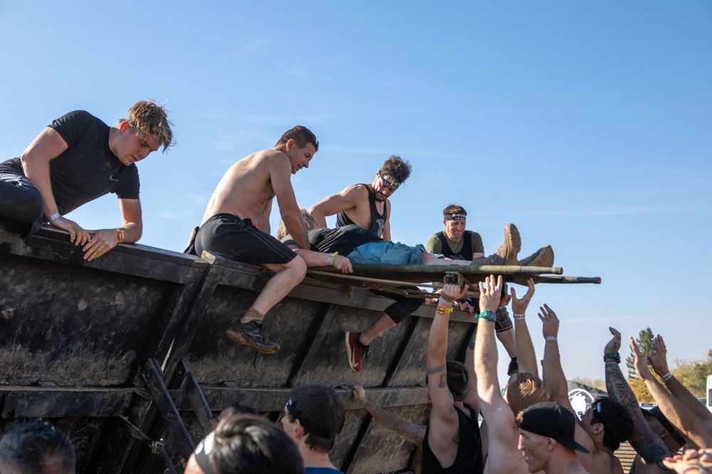 Participants helping others climb over a wooden obstacle during an outdoor event.