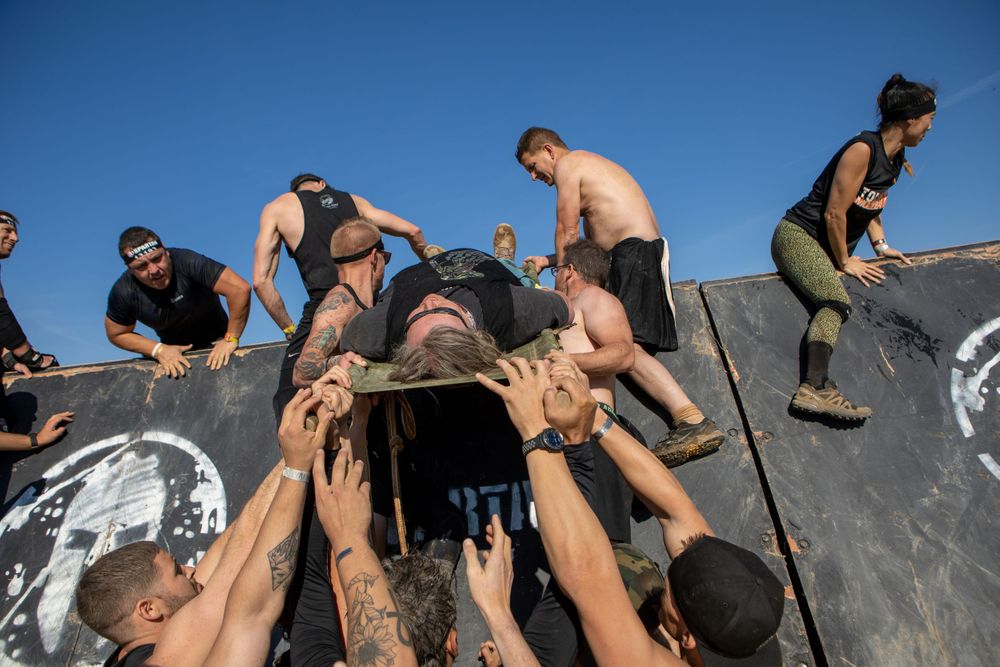 Athletes working together to help fellow competitors over a wall obstacle.