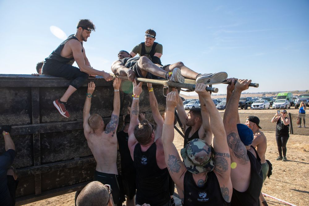 Team members collaborating to lift participants over a barrier during an obstacle course event.