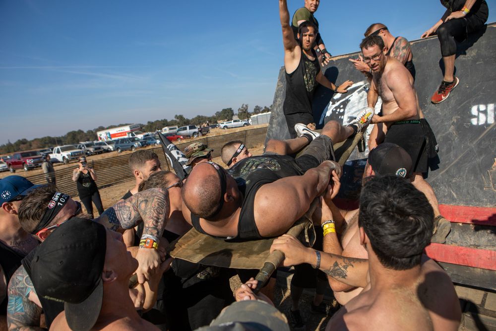 Participants climbing over obstacles at an outdoor obstacle course race event on a sunny day.