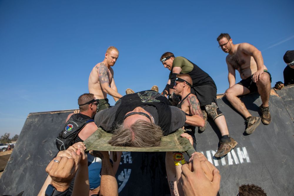 Athletes helping each other over a high wall obstacle during an outdoor race challenge.