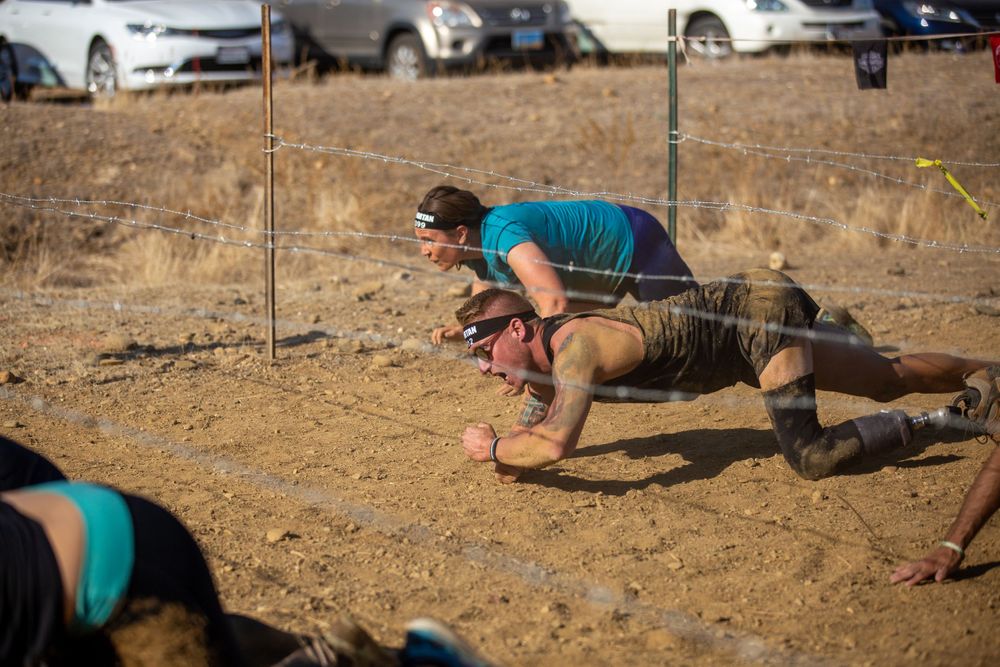 Athletes crawling through a challenging obstacle course section with barbed wire.