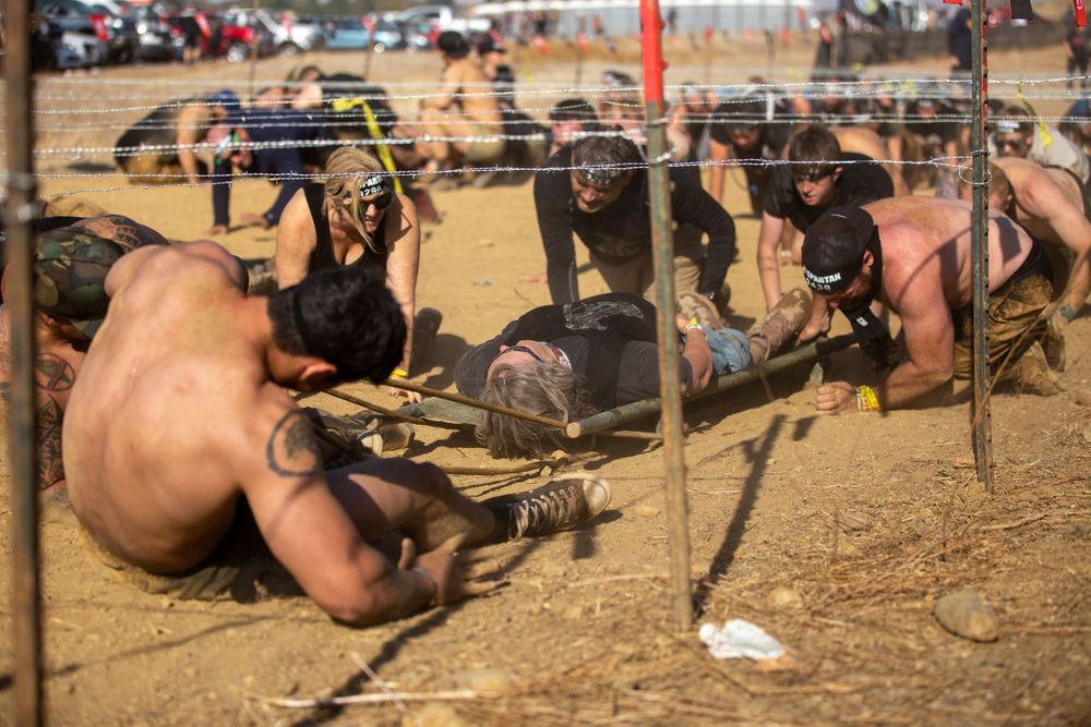 Participants navigating through a low crawl section at an outdoor obstacle race.