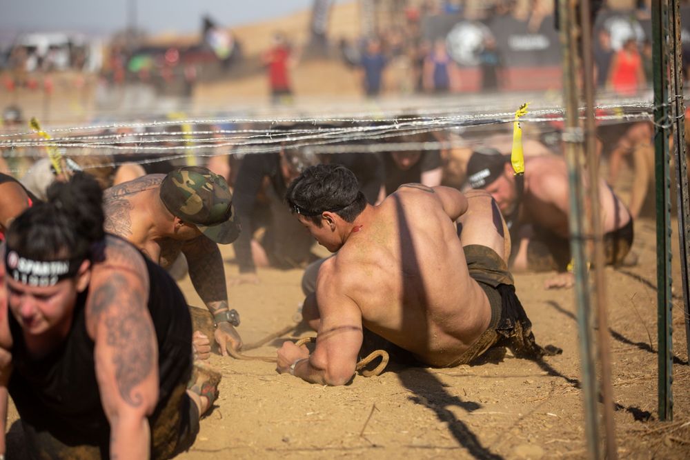 Participants crawling under wire obstacles during a challenging outdoor race.