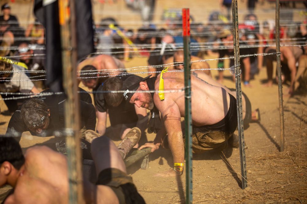 Competitors navigating through a barbed wire obstacle during an outdoor endurance race.