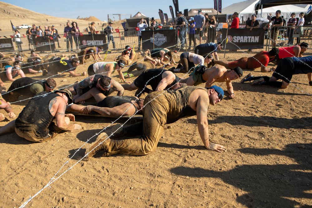 Participants crawl through a military-style obstacle course during an outdoor endurance event.