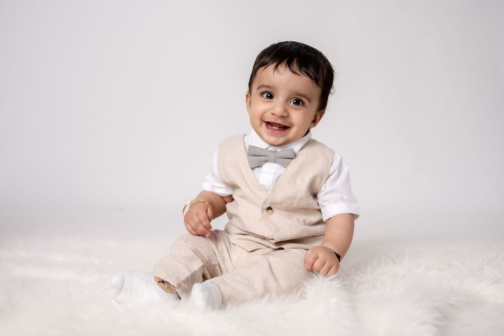 Smiling baby in formal wear posing on wooden crate against white background.