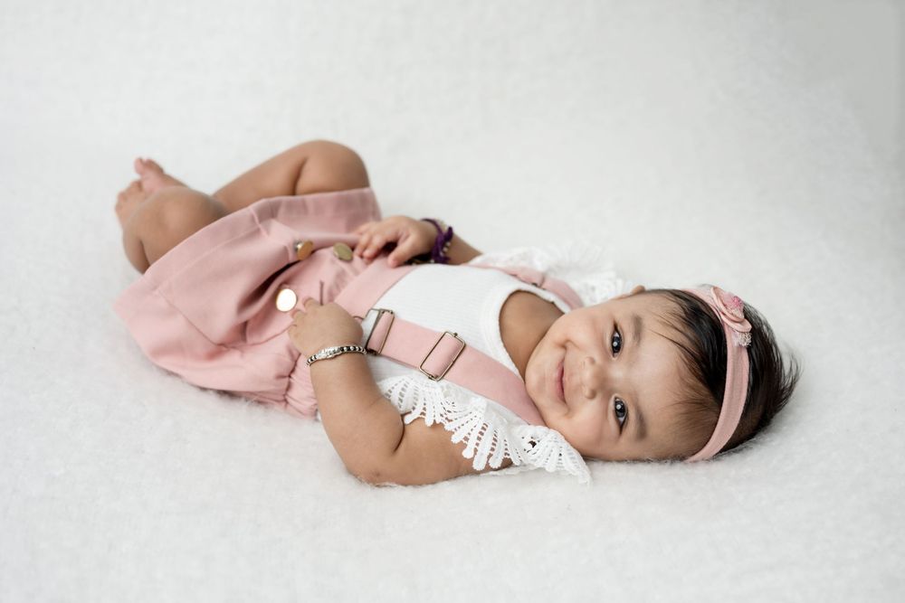 Baby in light colored outfit lying on soft white fabric during professional photoshoot.