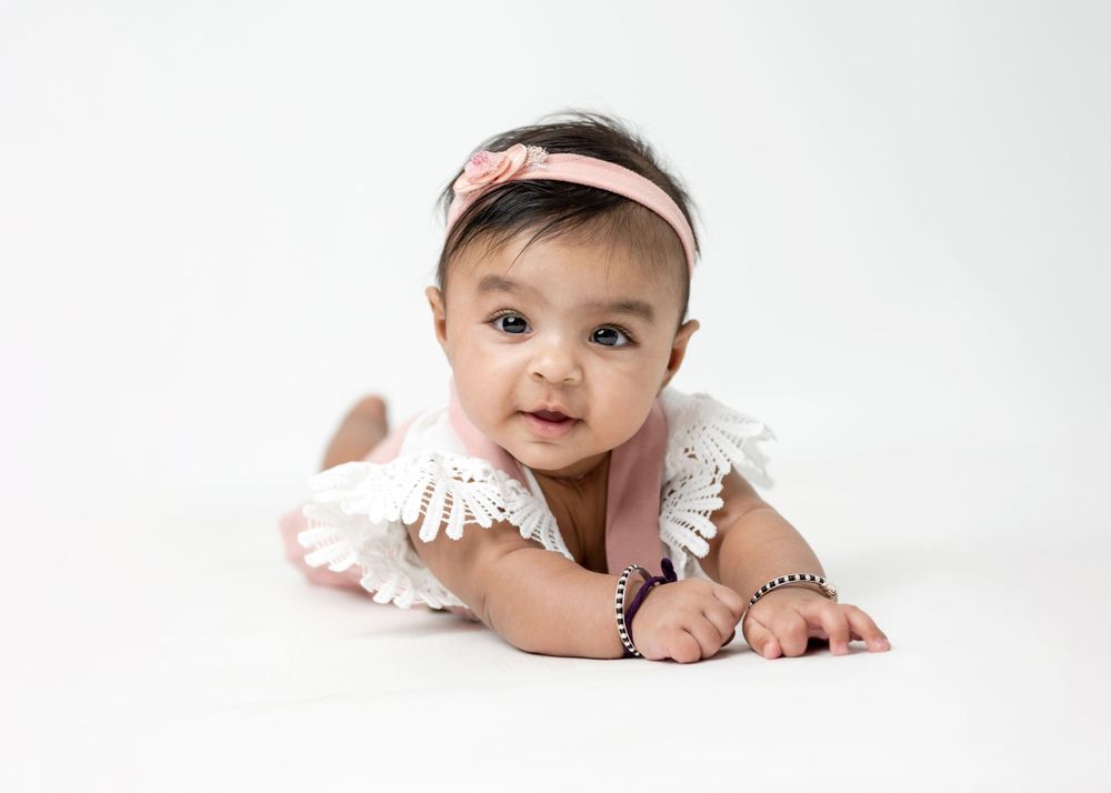 Baby in white outfit lying on stomach during professional photo session.