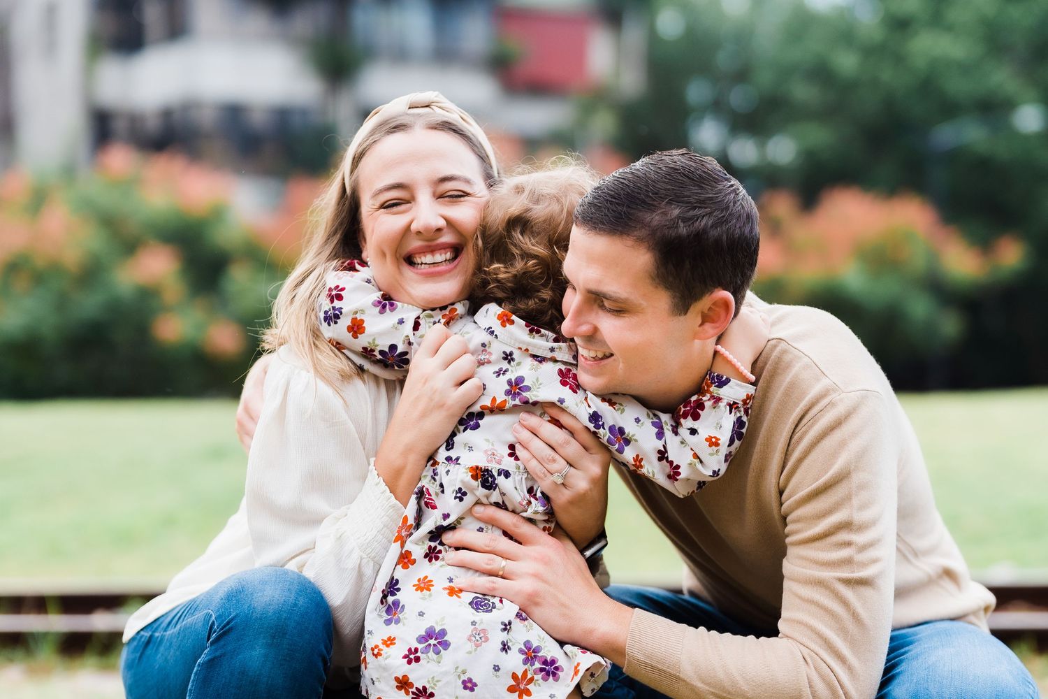 Family having fun outdoors while cuddling their young child in a floral dress.