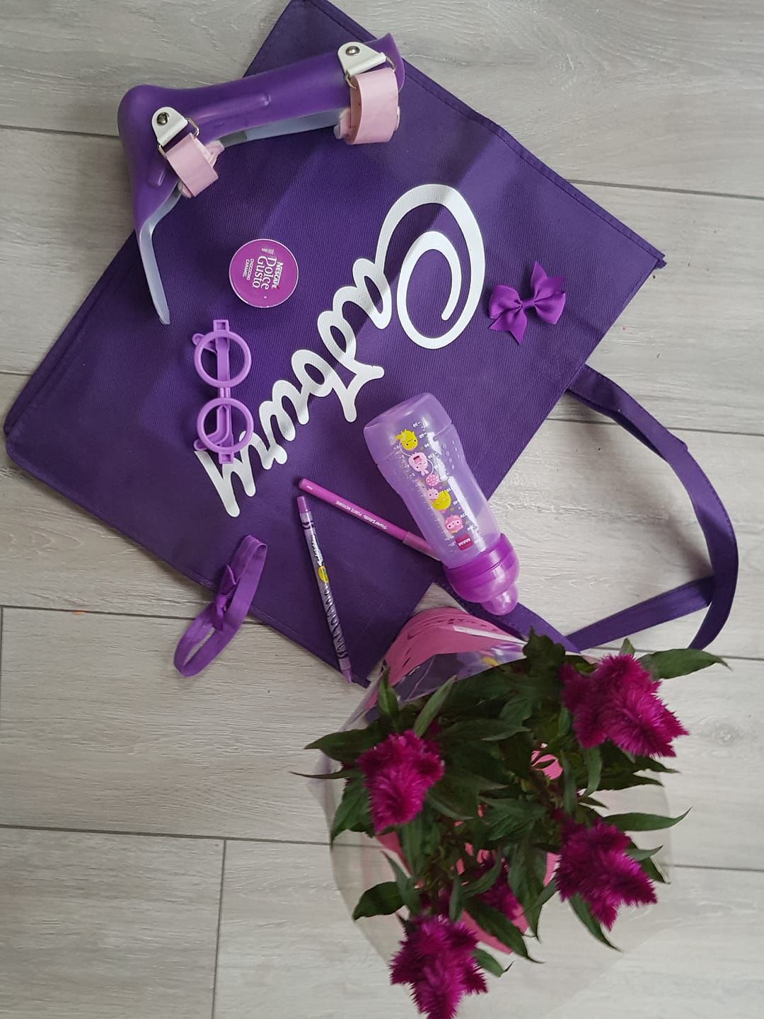 Purple tote bag with floral accents and matching accessories arranged on a gray wooden floor.
