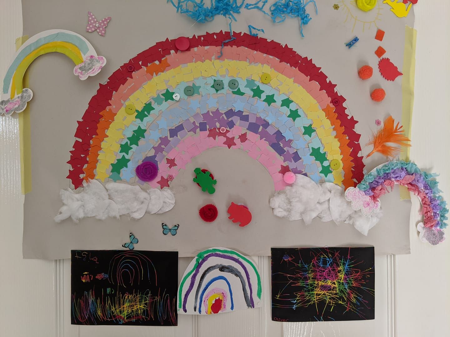 Colorful rainbow artwork with clouds displayed on a wall above black paper drawings.