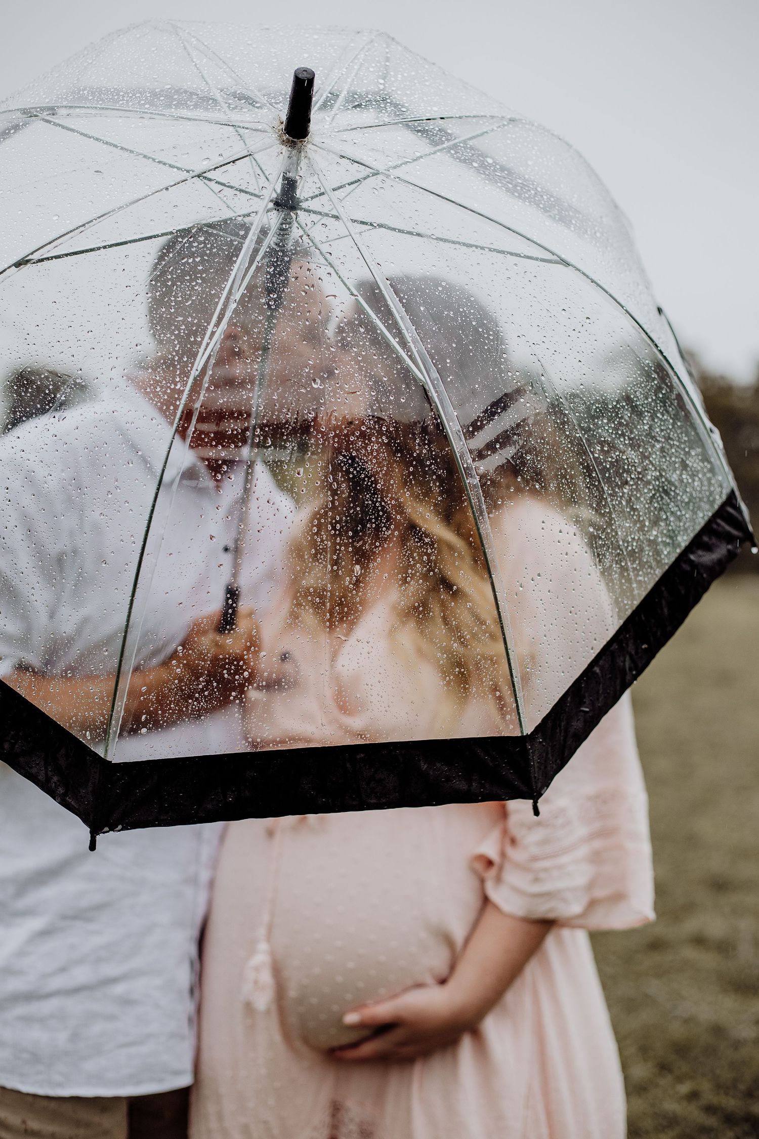 A couple shares an intimate moment under a clear umbrella on a rainy day.