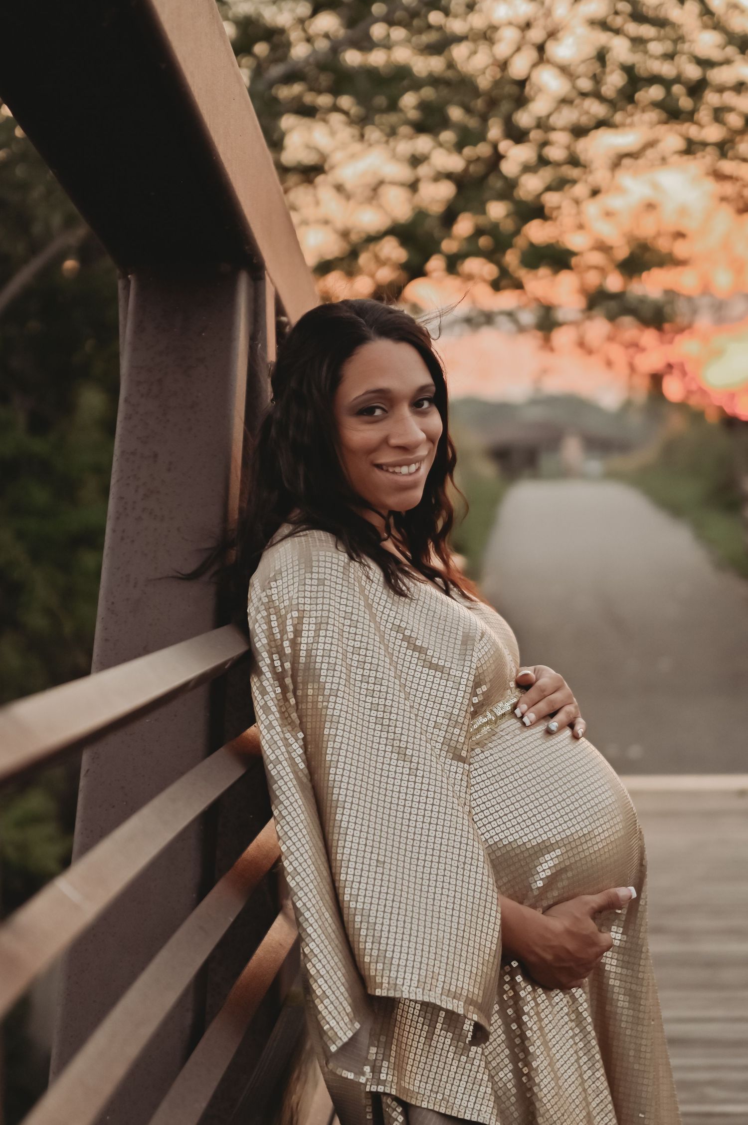 A sunset maternity photo on a wooden bridge with warm lighting.