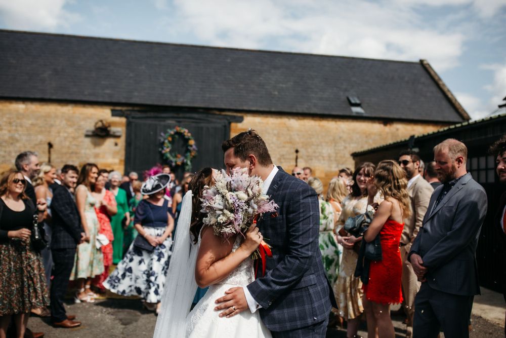 Newlyweds share romantic moment surrounded by celebrating guests outside stone venue.