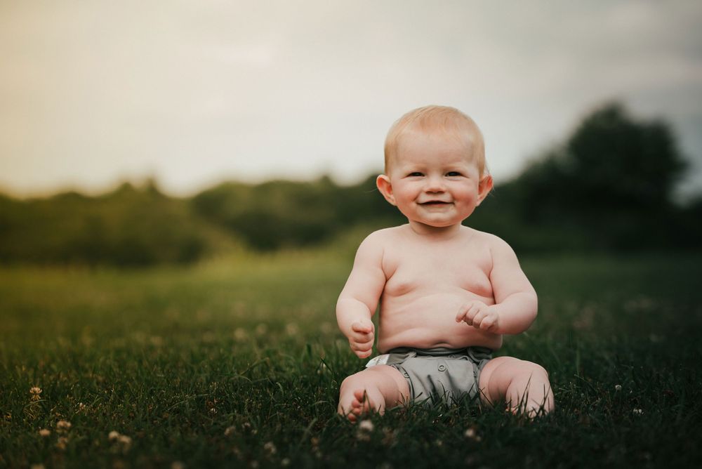 Happy baby sitting on green grass outdoors in summer light.