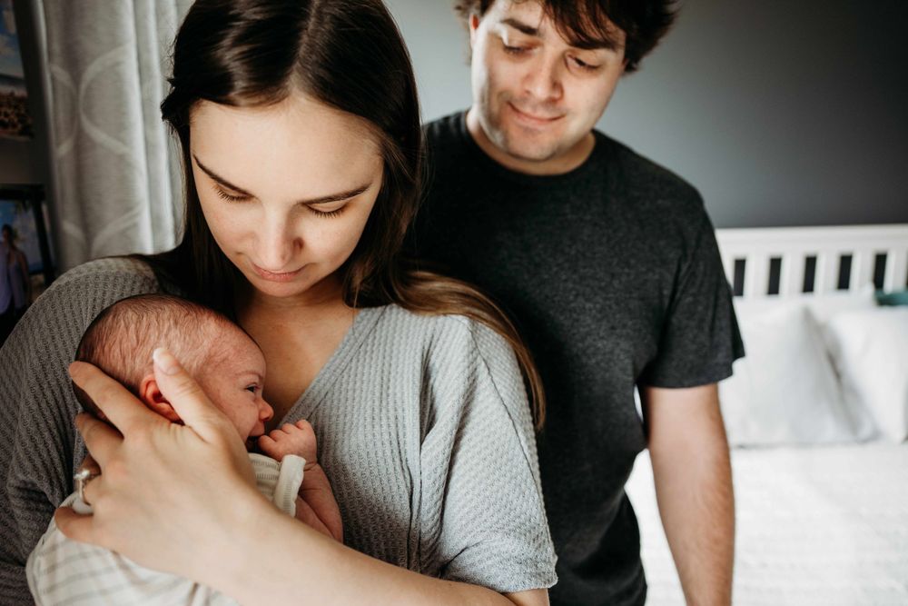 New parents smiling and cradling their sleeping newborn baby together.