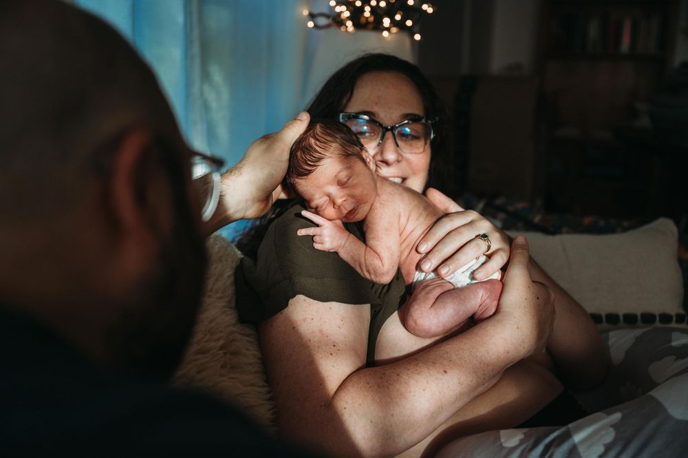 Two parents lovingly hold their newborn baby together in a softly lit bedroom.