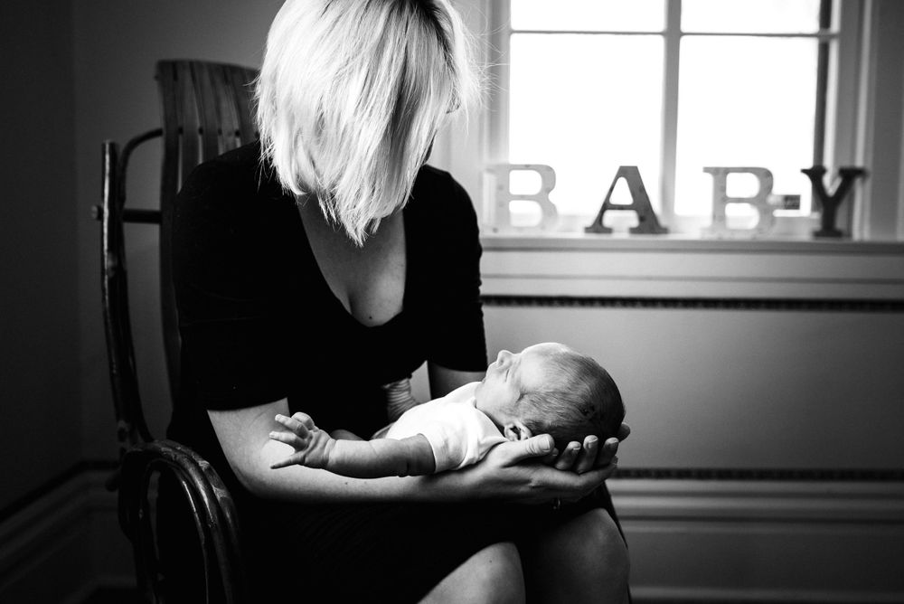 Black and white photo of a mother sitting in a chair cradling her sleeping newborn baby.