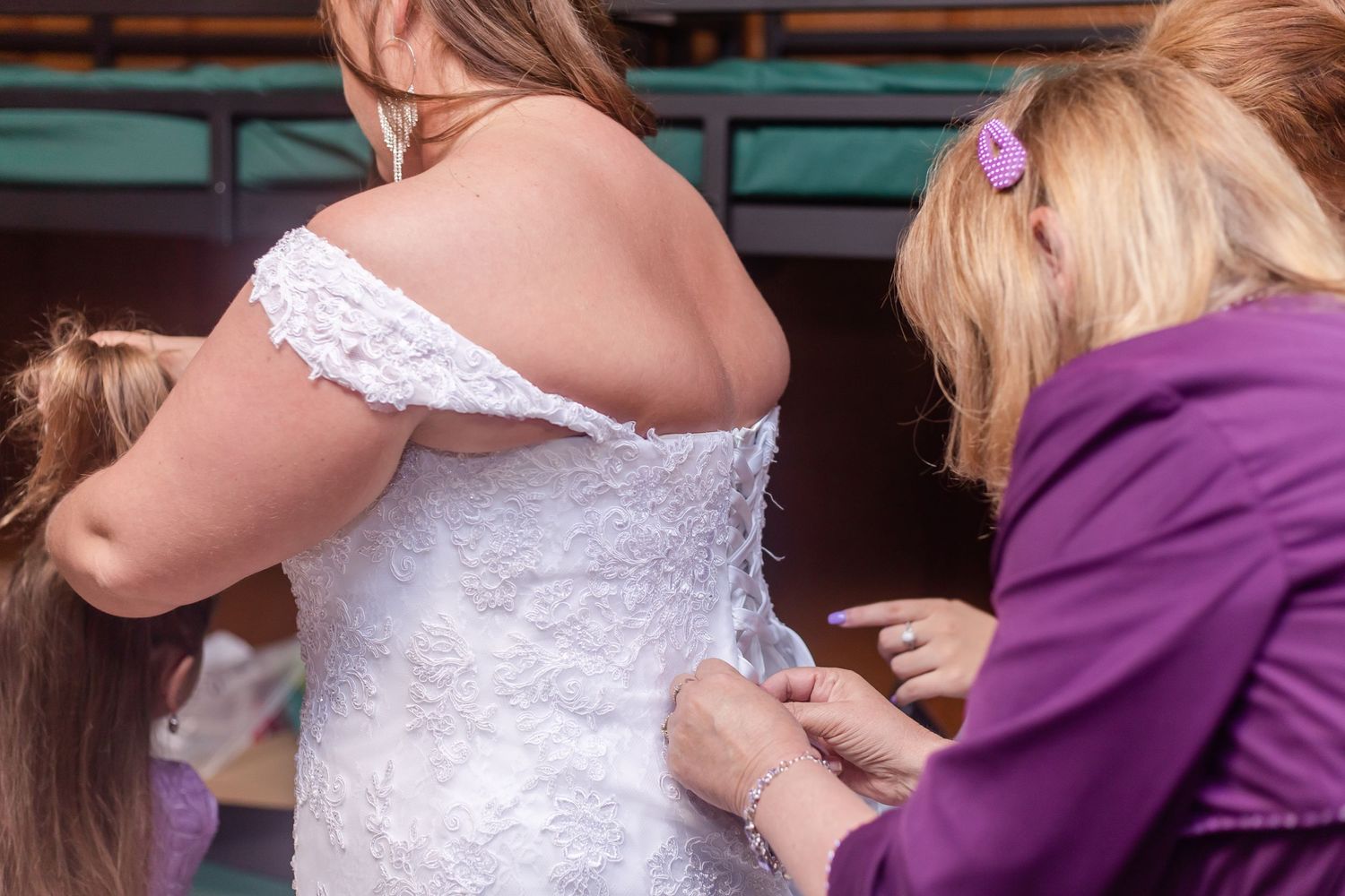 Wedding party members help with final dress adjustments in purple and white attire.