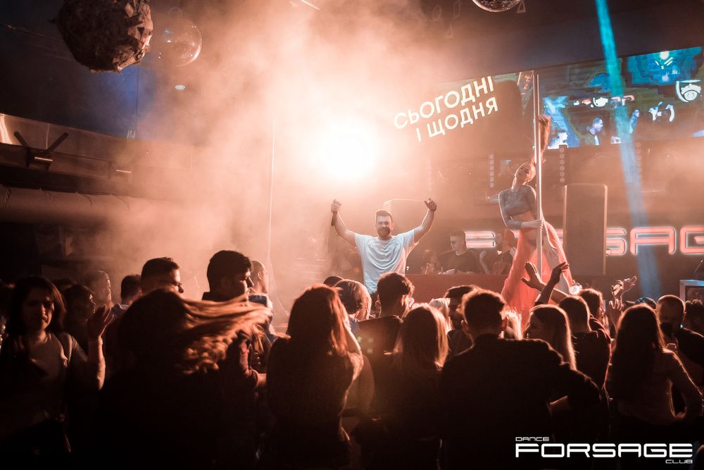 Crowded nightclub scene with performer on stage and audience silhouettes in foreground.