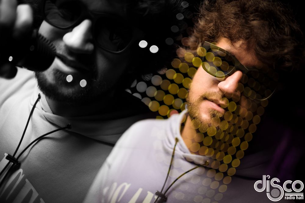 DJ wearing glasses photographed in black and white with honeycomb pattern overlay.