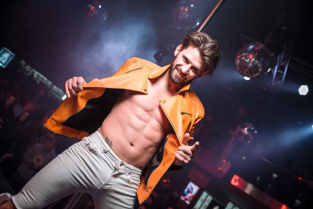 Energetic nightclub scene with colorful lighting and performers on stage creating a vibrant party atmosphere.
