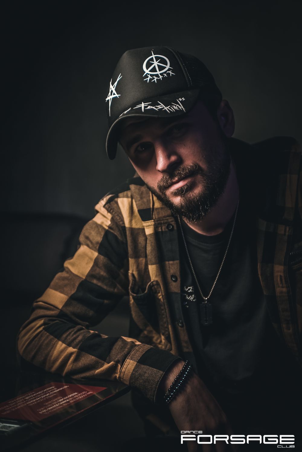 Portrait of person wearing peace symbol cap in moody lighting with brown checkered jacket.