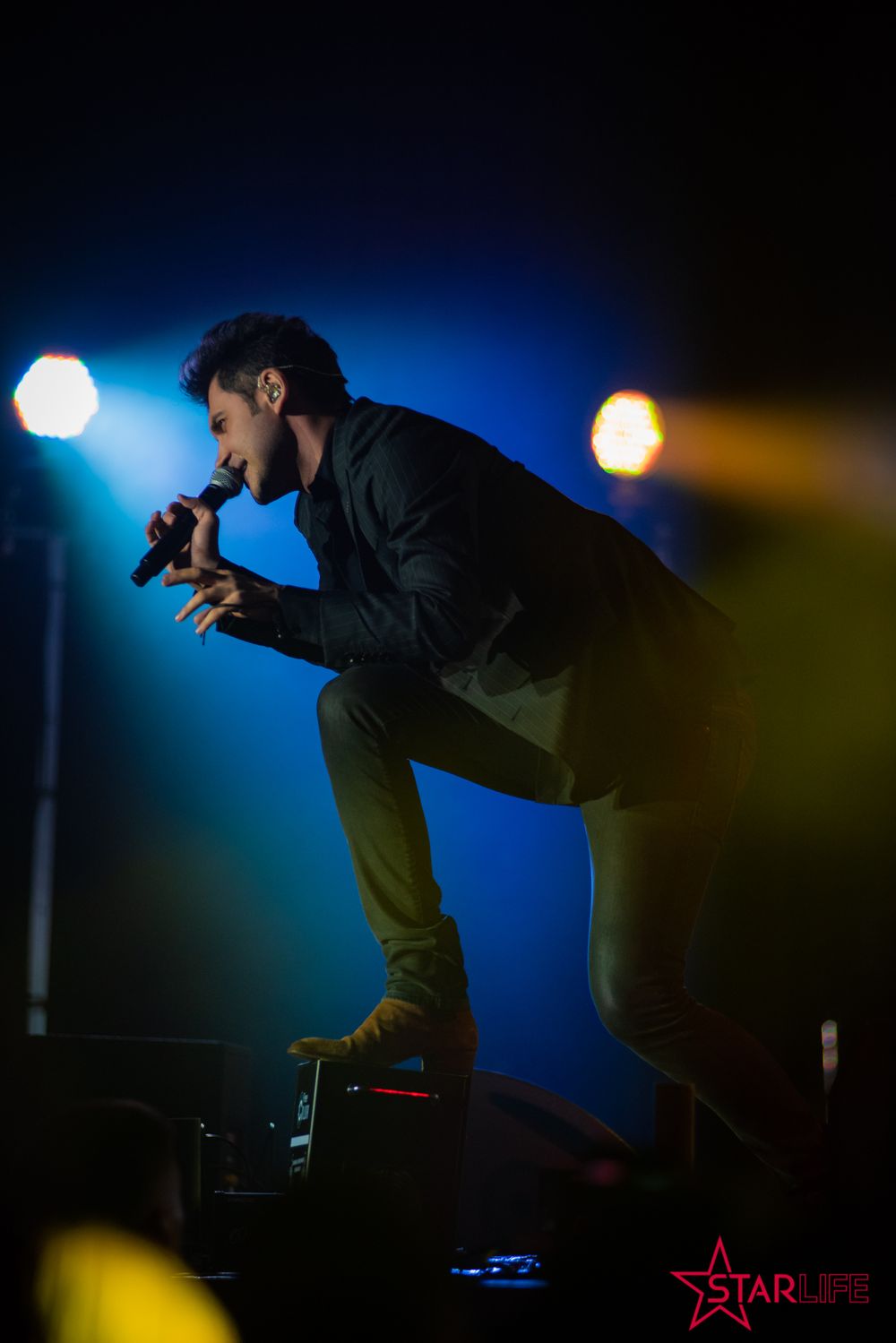Silhouetted performer bending forward on stage with dramatic blue and yellow lighting.