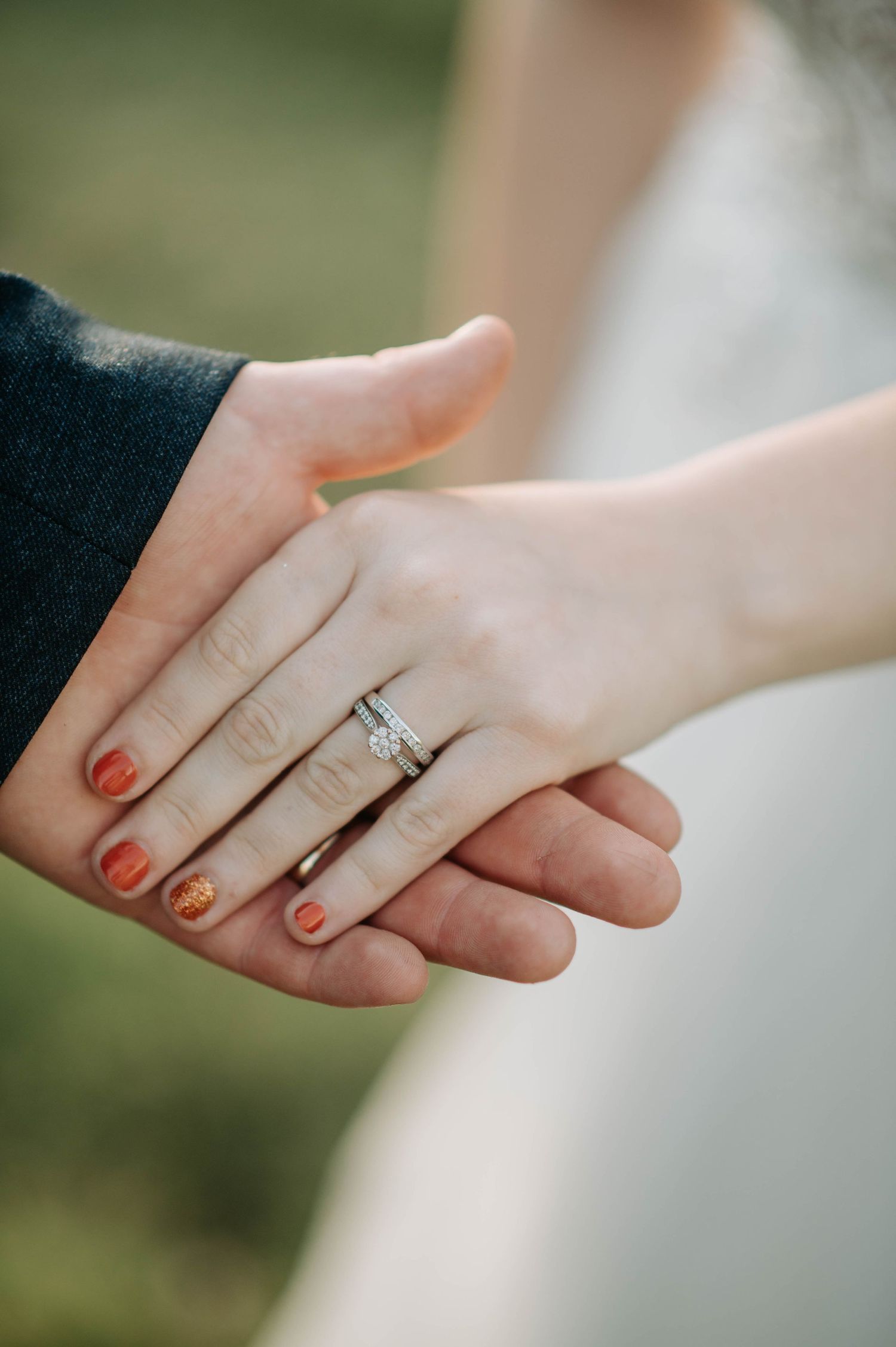 Close up detail of wedding rings and joined hands with red nail polish.