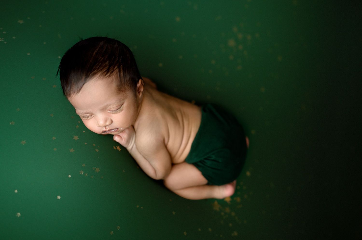 A peaceful sleeping newborn posed against a dark green background during a professional photo session.