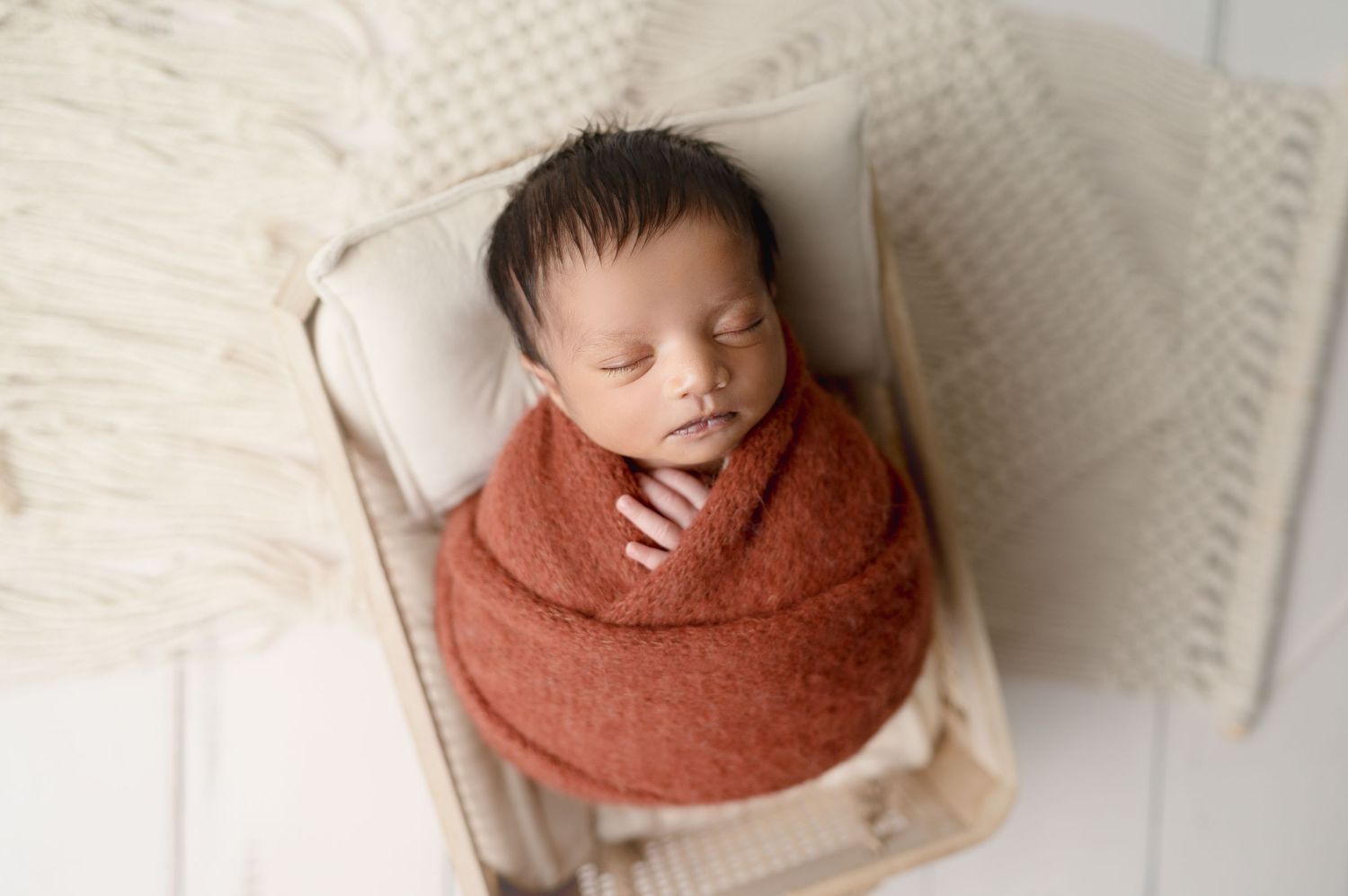 Sleeping newborn wrapped in rust colored swaddle on white textured chair.