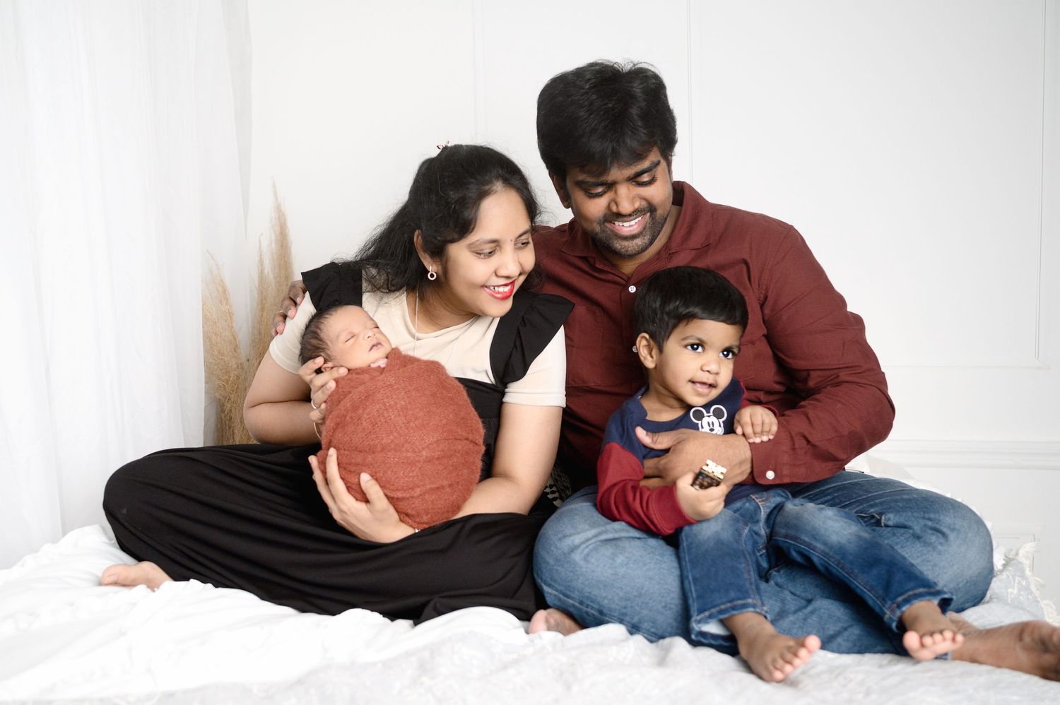 Happy family sitting together on bed for portrait with newborn and toddler.