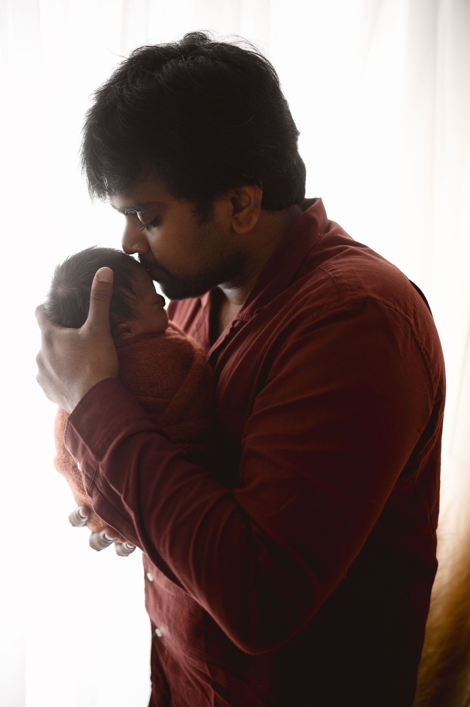 An intimate bonding moment between parent and newborn in silhouette against window light.