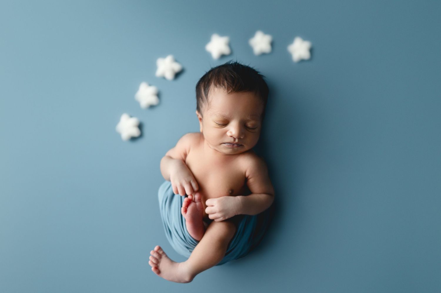 Newborn wrapped in blue fabric sleeping peacefully with white stars decoration.