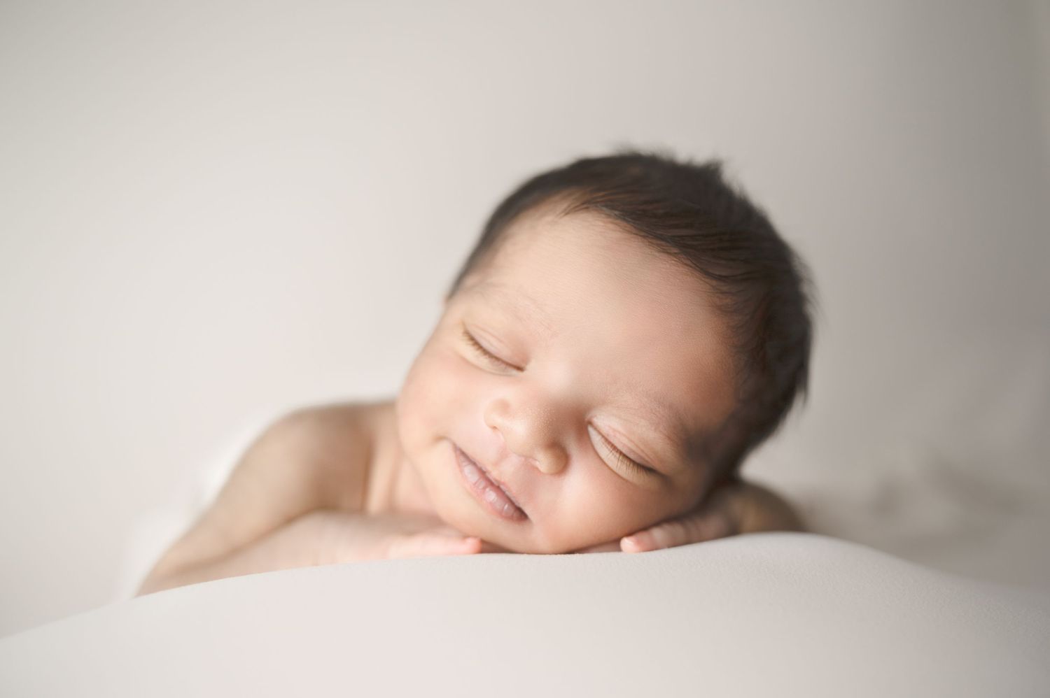A peaceful newborn baby with dark hair resting on white bedding during a photo session.