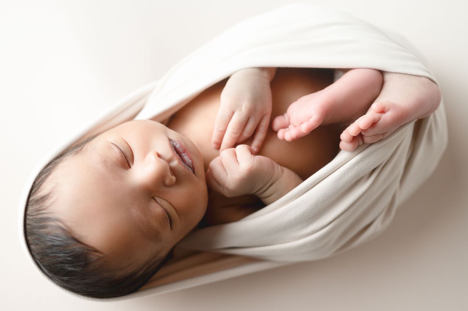 A sleeping infant wrapped in soft white fabric during a minimalist portrait session.