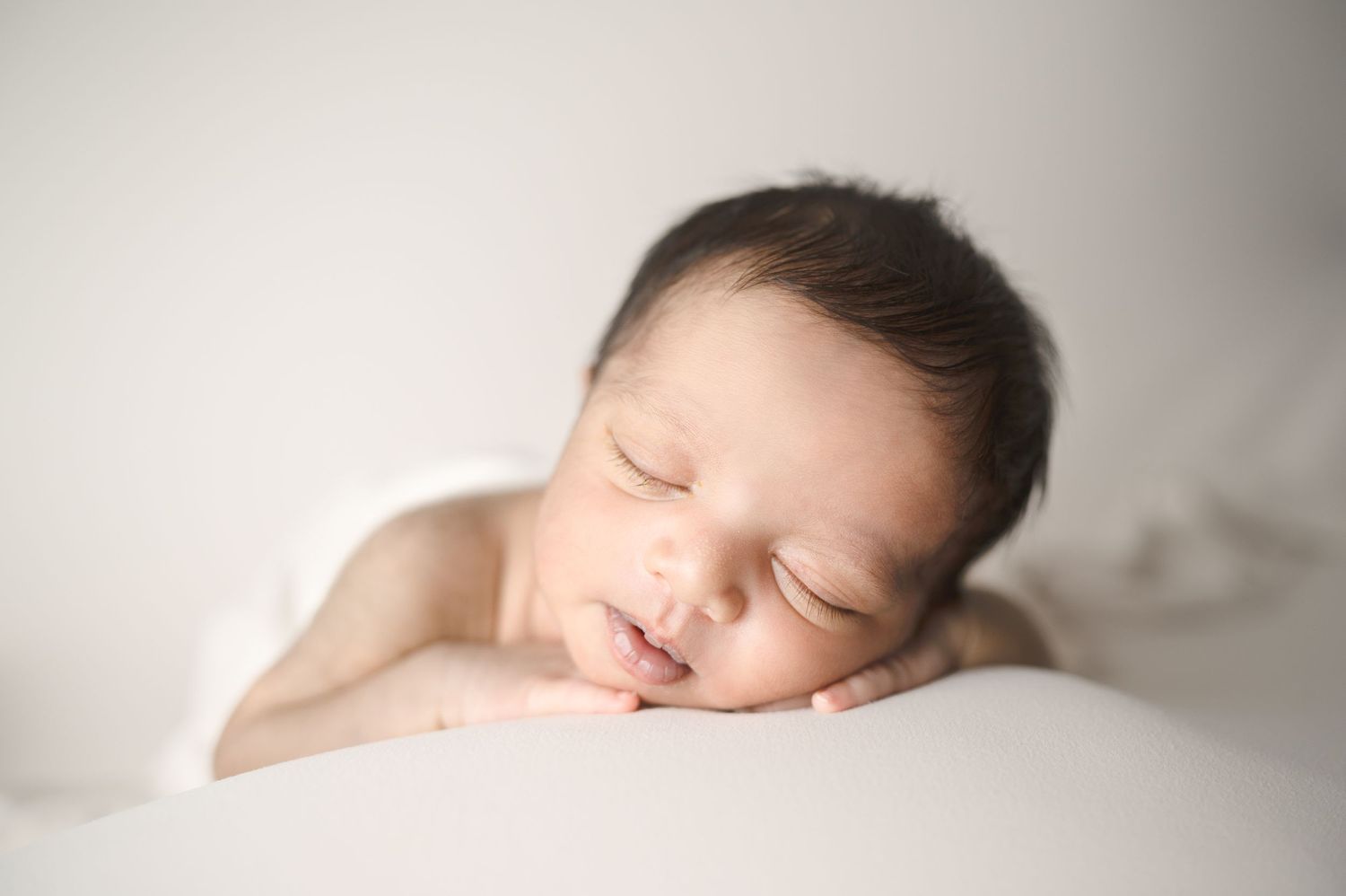 A serene newborn baby sleeping on soft white fabric during a professional portrait session.