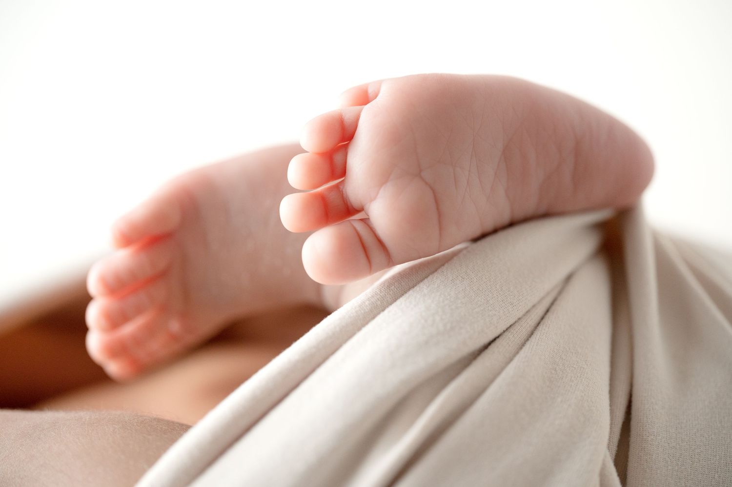 Small baby feet peeking out from under white fabric during an intimate newborn photo session.