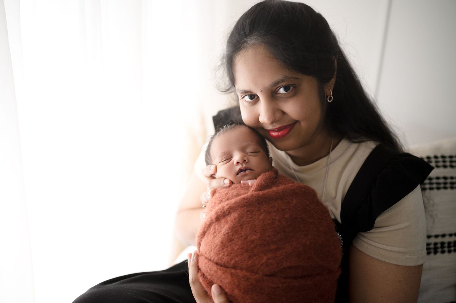 A joyful parental moment with a swaddled sleeping newborn against a bright background.