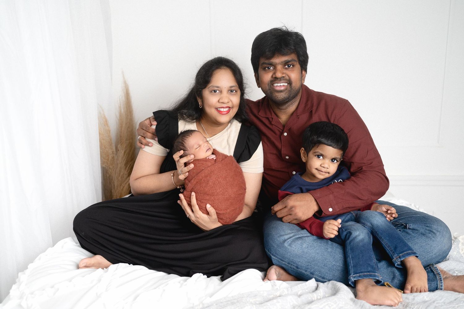 Family of four posing together on white bed for intimate portrait session.