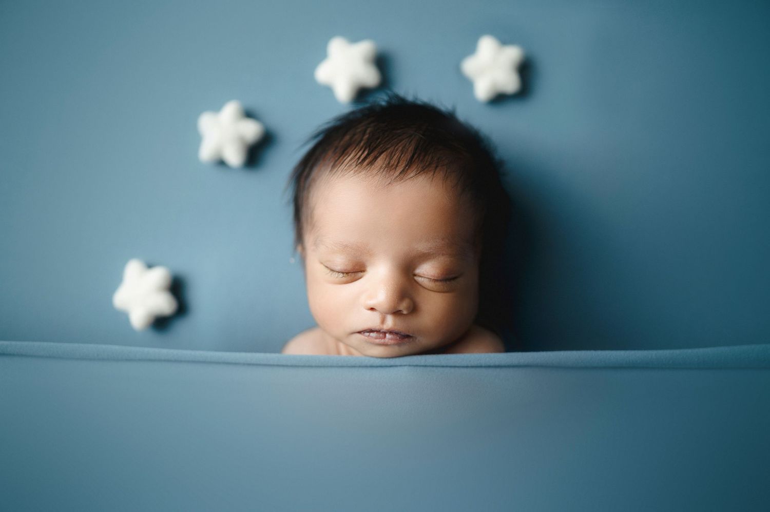 Sleeping newborn peacefully resting against blue backdrop with white stars.