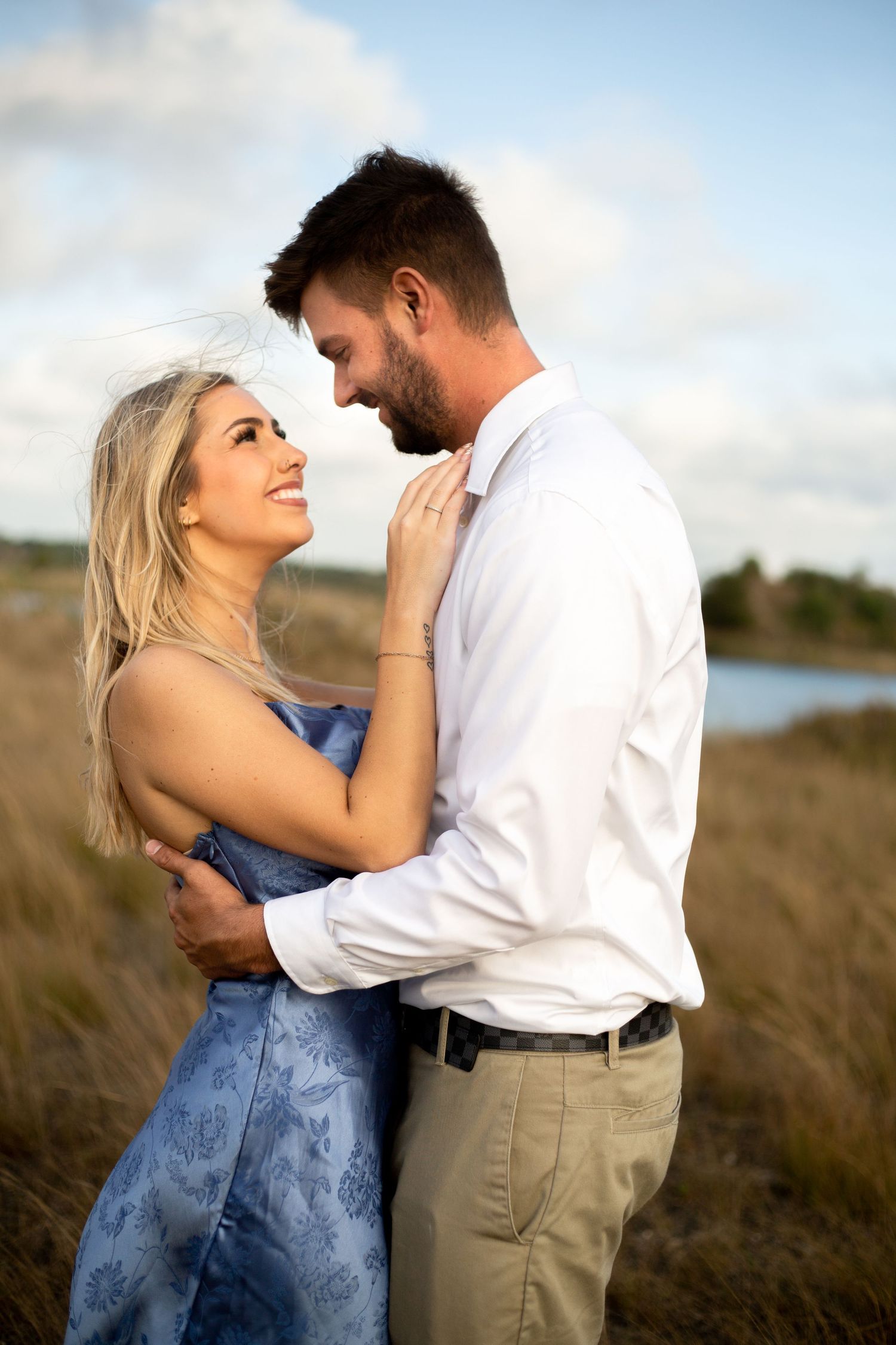 Couple in formal attire share romantic moment in coastal field setting.