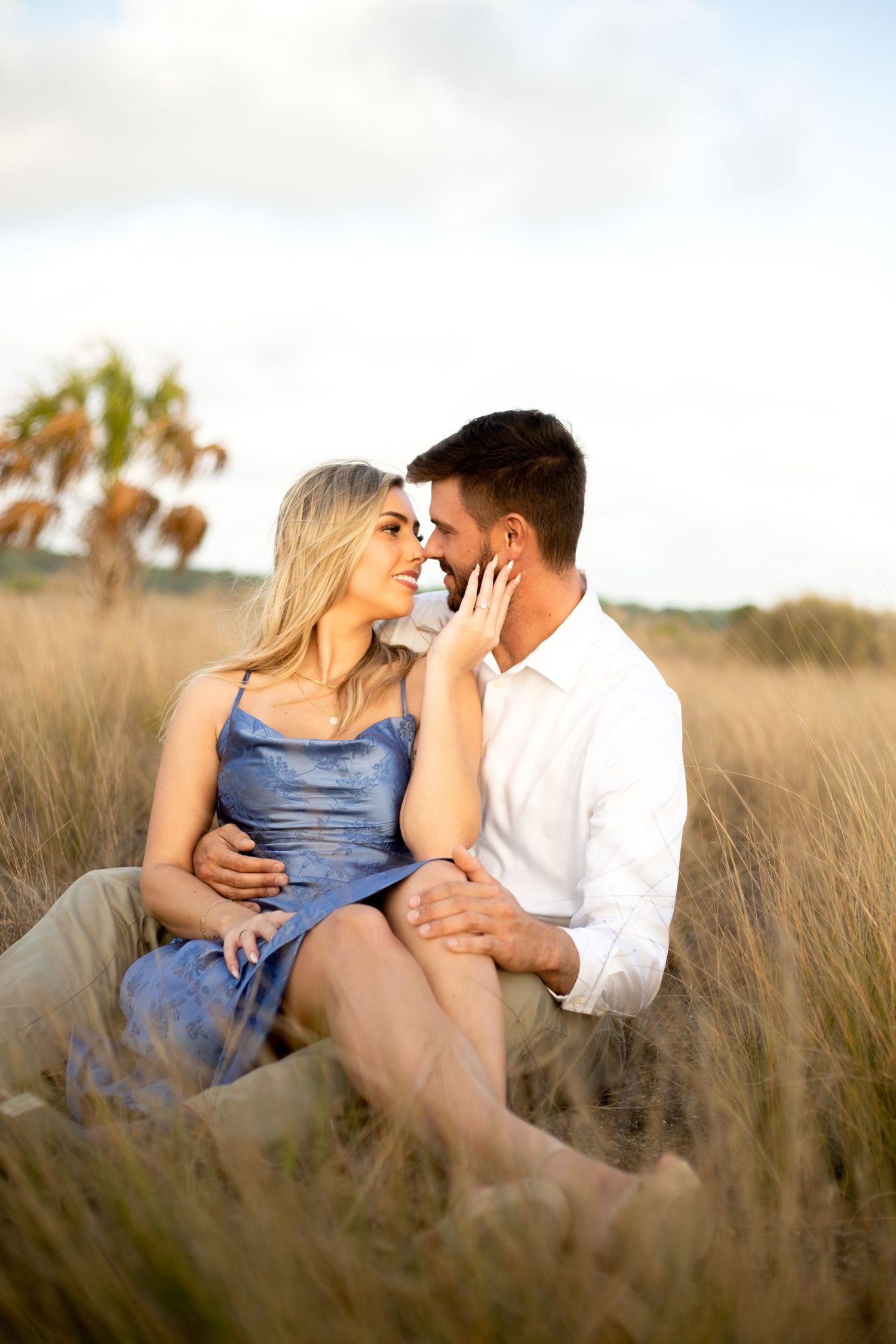 Intimate couple sitting in tall grass during golden hour near palm trees.