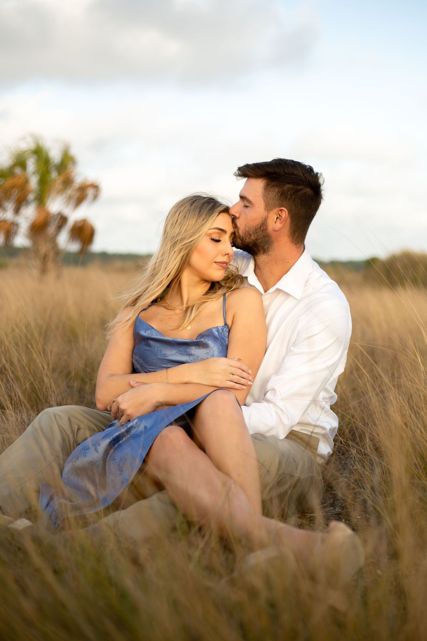 Couple sharing tender moment while sitting in golden field at dusk.