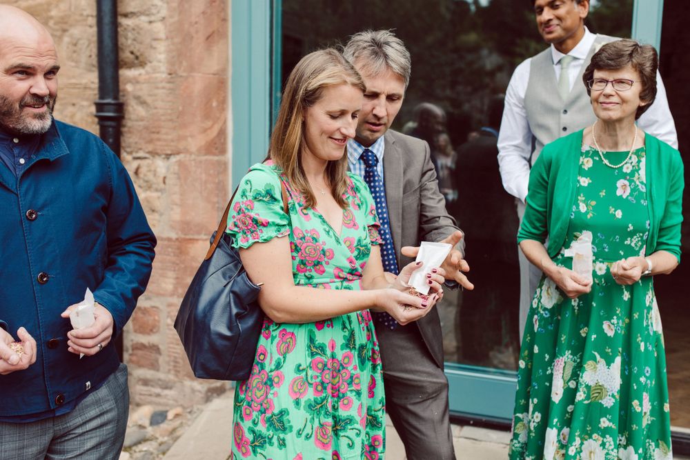 Wedding guests in colorful attire gathered outside a stone building with turquoise trim.