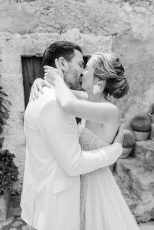 Romantic black and white wedding portrait shows couple embracing against stone wall.