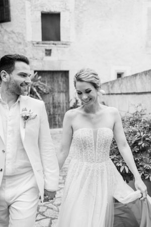 Newlyweds in white attire share a joyful moment while walking together.