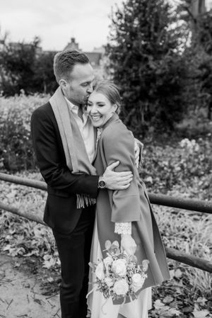 Romantic autumn engagement photo with couple embracing outdoors holding floral bouquet.